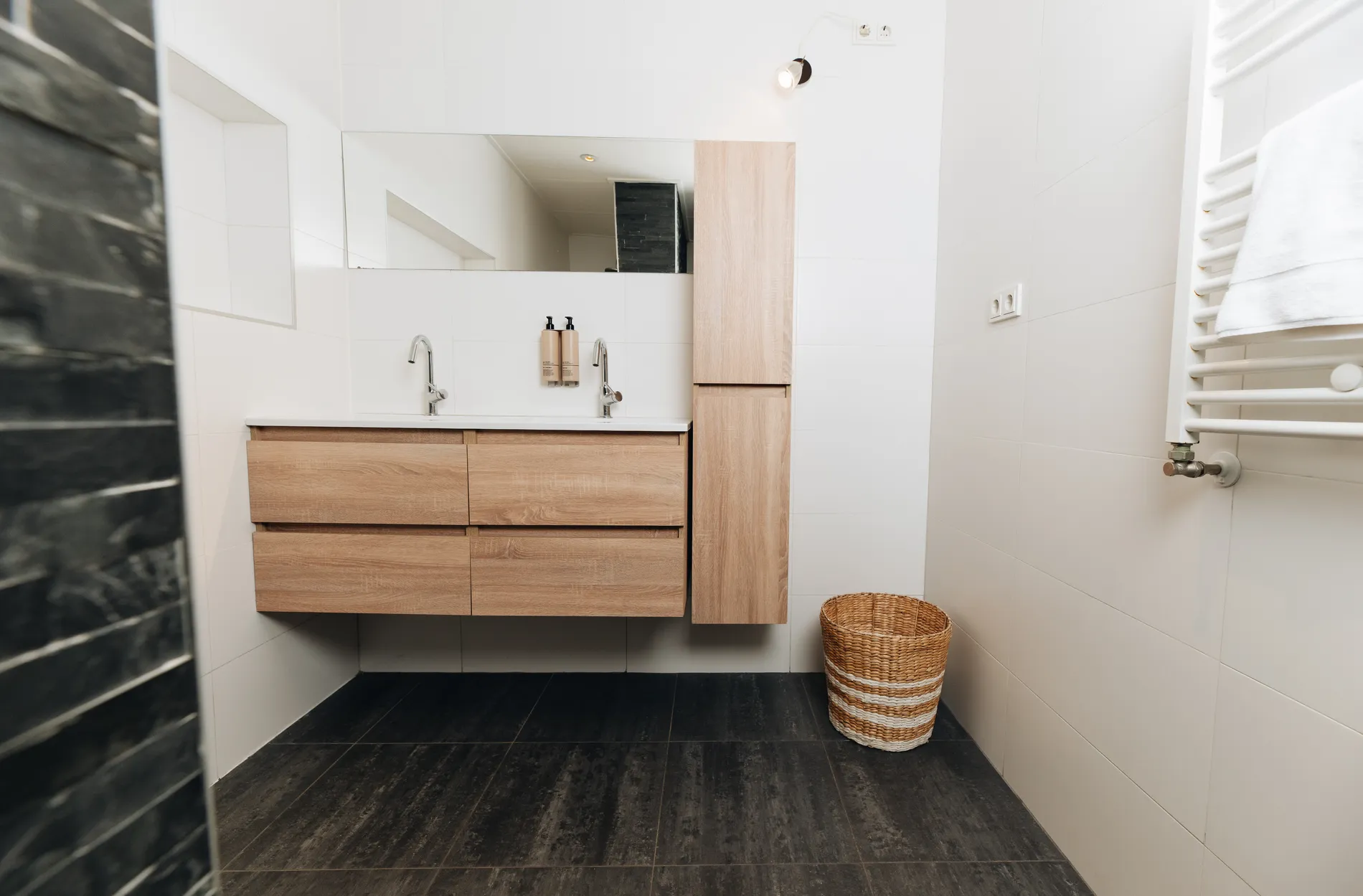 Ruime en luxe badkamer voorzien van een dubbel houten wastafelmeubel en grote spiegel.